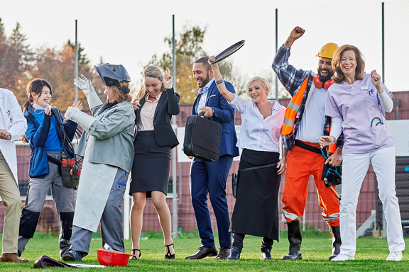 A cheerful group of people in various professional outfits celebrate together, symbolising unity and diversity in working life.