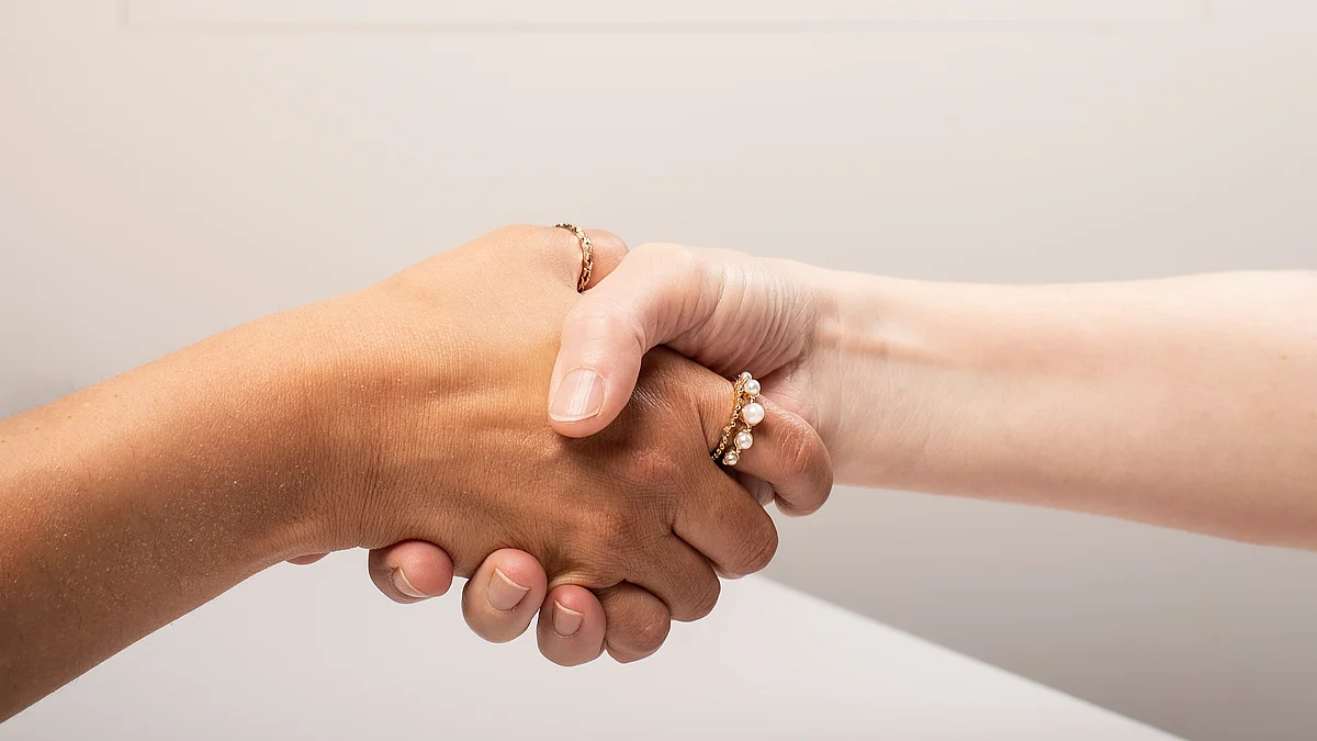 Two hands of different skin tones shaking hands, one wearing gold rings, symbolising unity and cooperation.
